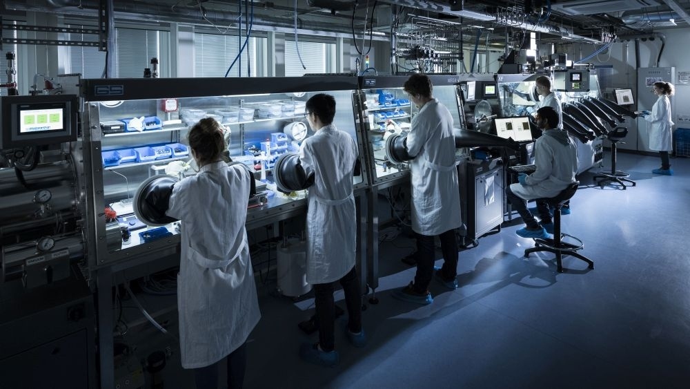 Scientists in lab coats working with glove boxes and advanced scientific equipment in a laboratory.